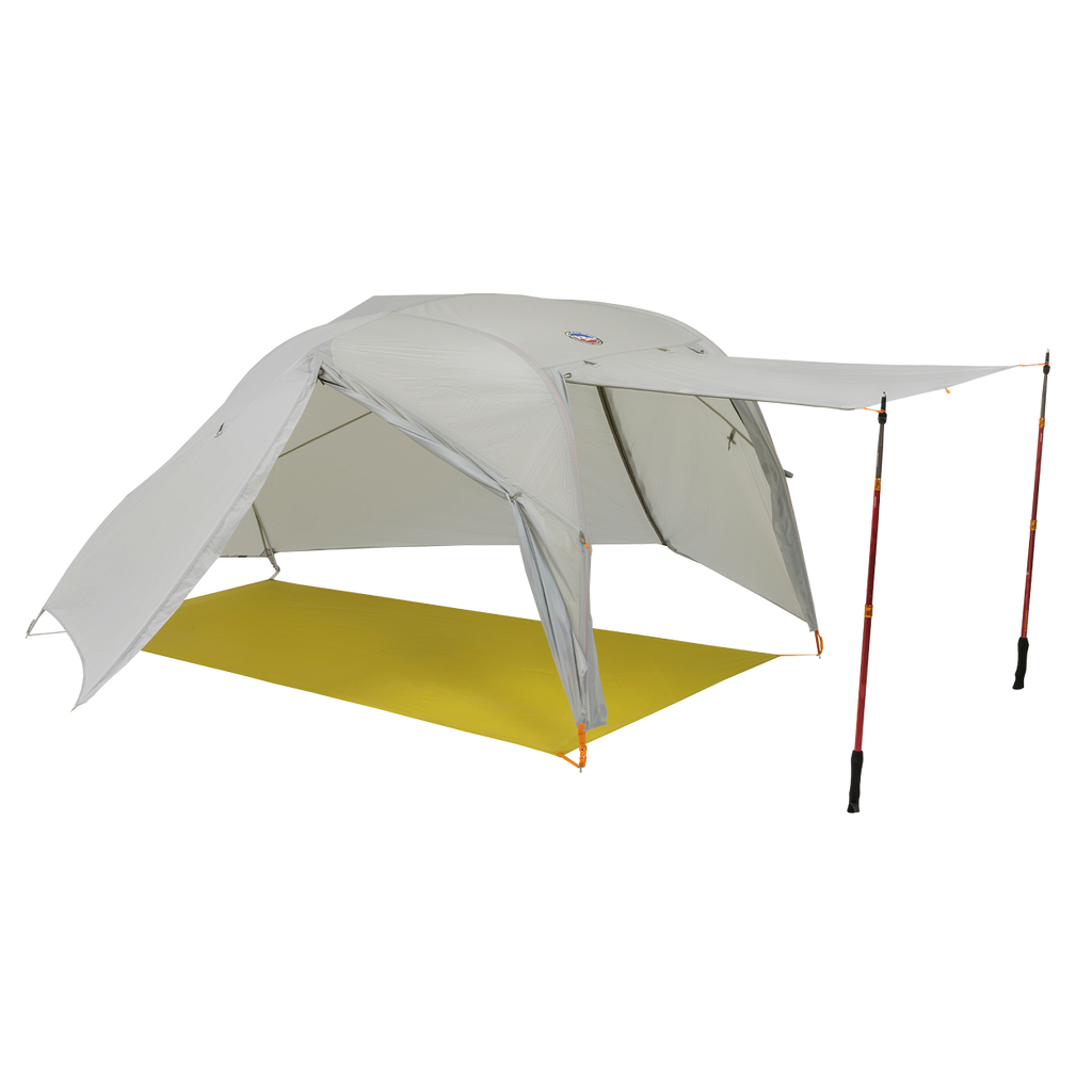 The Big Agnes Salt Creek 2, a light gray backpacking tent, is shown with one side propped open by trekking poles for an awning and panoramic views, set up on a bright yellow groundsheet.