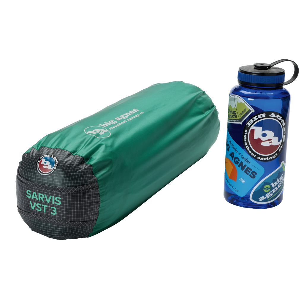 A green, cylindrical Big Agnes Sarvis VST 3 tent bag made with Hyperbead fabric is next to a blue Big Agnes water bottle with outdoor stickers on a white background.